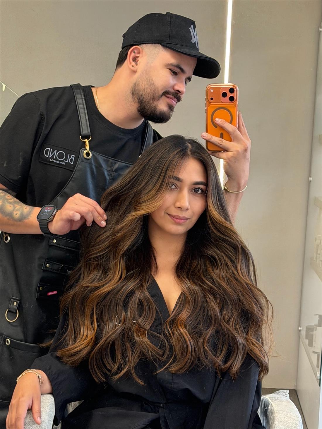 Clienta con ondas castañas y luces caramelo, con su estilista detrás