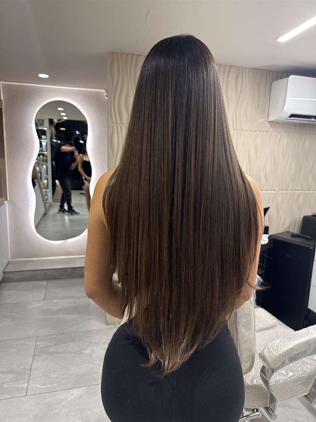 Cabello castaño muy largo y liso, de espaldas, frente a un espejo con luz
