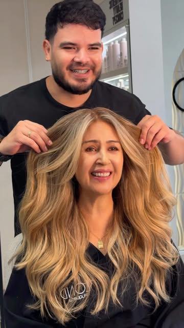 Clienta sonriente con rubio vainilla en ondas, con su estilista detrás